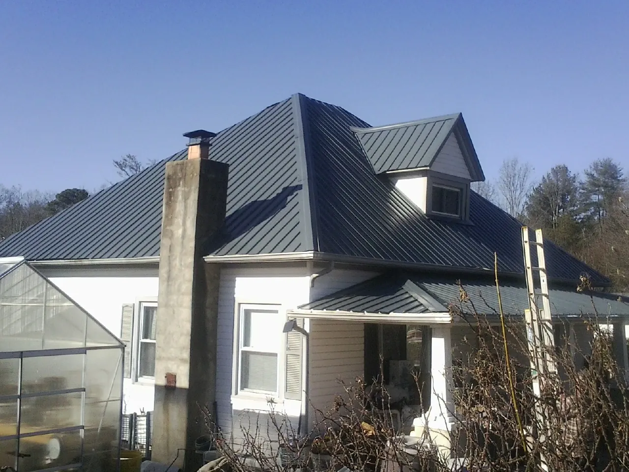 Dark blue standing seam metal roof on a white farmhouse with dormer — Slate & Tile Roof Repair by Roofing Brothers in Port Clinton