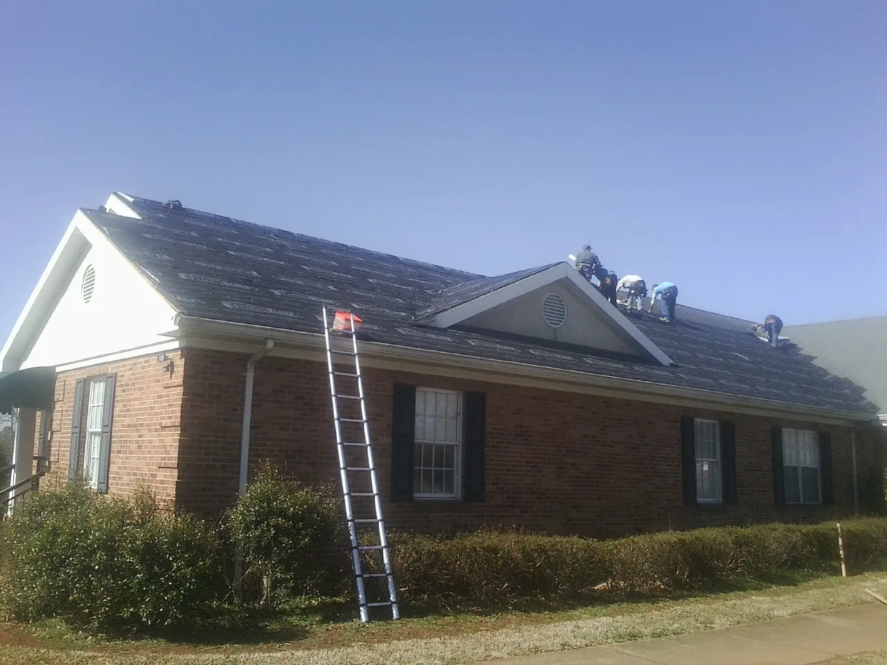 Crew tearing shingles off a brick ranch roof with a ladder set — Metal Roof Repair work by our crew in Port Clinton