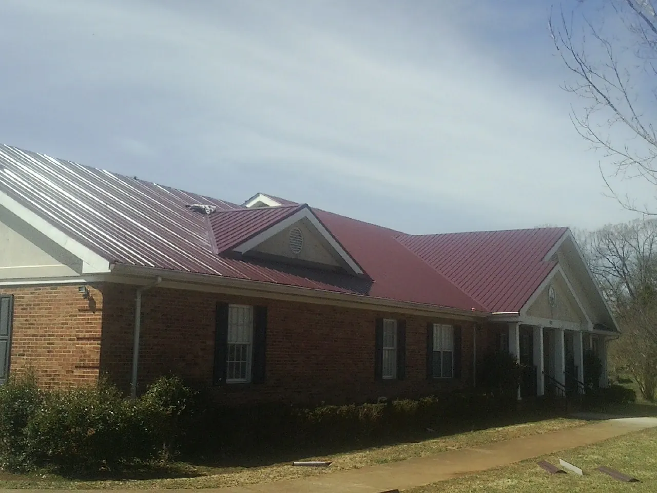 Red metal roof with gabled entries on a long brick building, from a Hail Damage Roof Repair job in Port Clinton