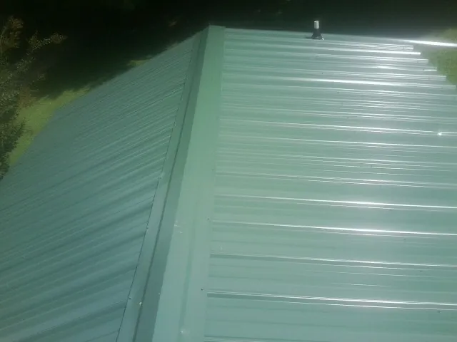 New green metal panels meeting at the ridge of a roof — Flat Roof Repair work by our crew in Port Clinton