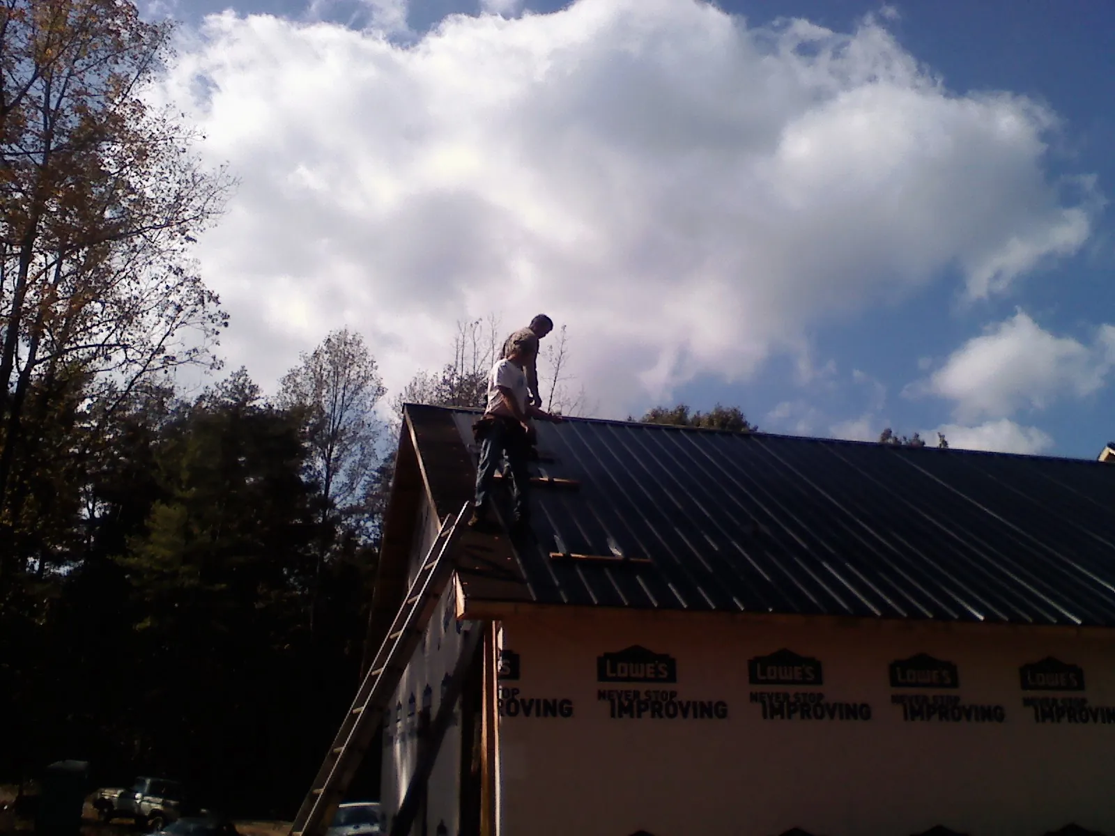 Roofer fastening dark metal panels high against a cloudy sky, from a Roof Inspection job in Port Clinton