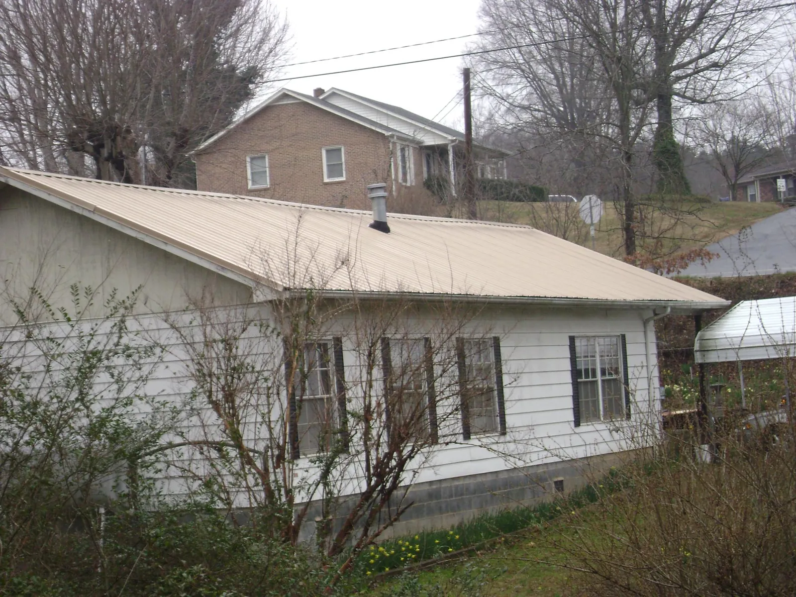 Tan metal roof on a white sided house set into a hillside — Commercial Roofing by Roofing Brothers in Port Clinton